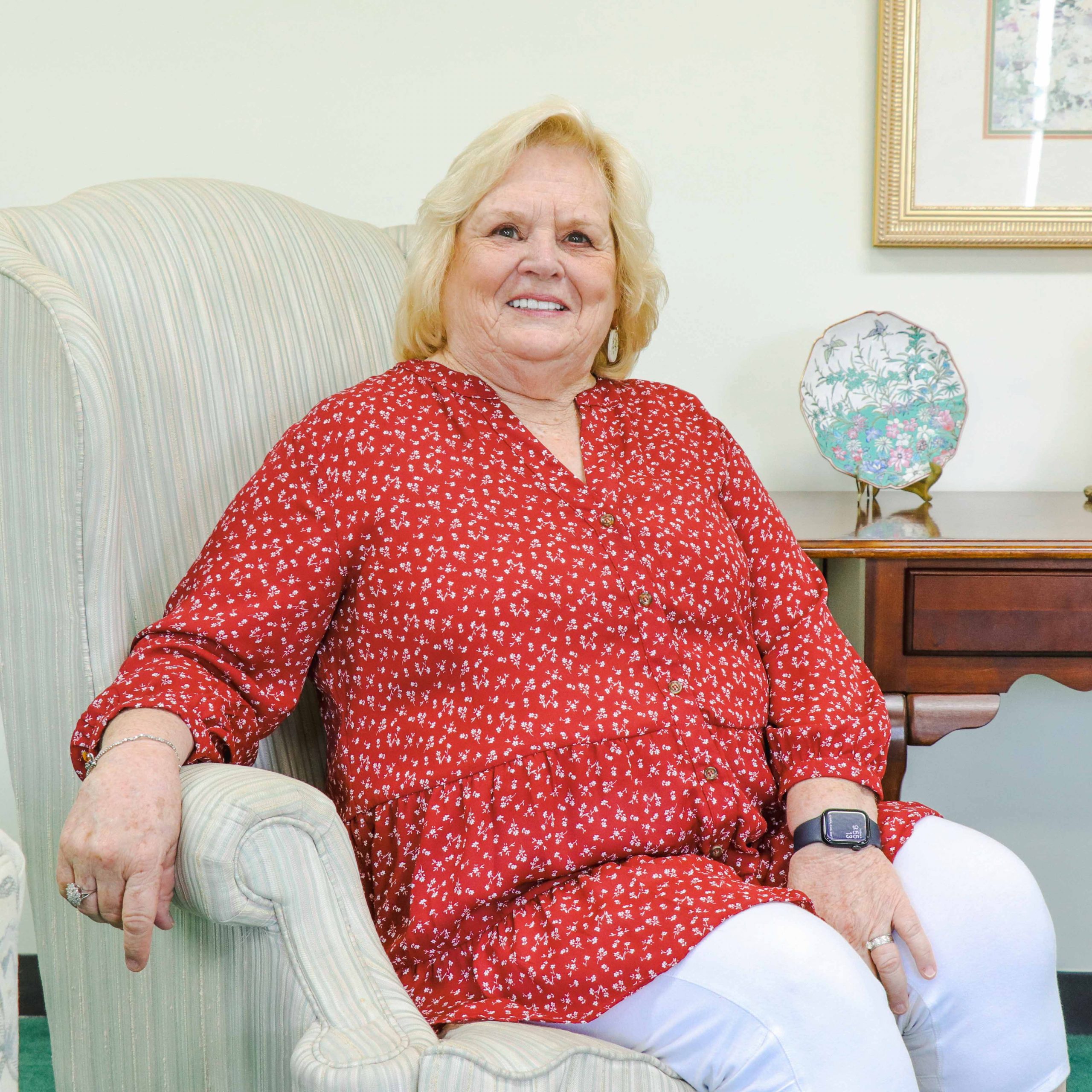 Betty Marlor is the SABQG president wearing a red spotted blouse and sitting in a cozy chair